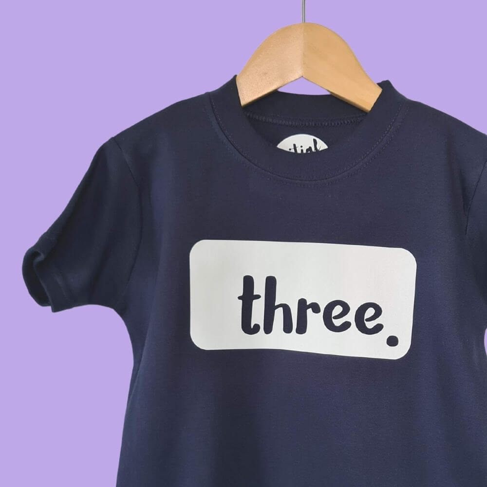 Hanging navy blue t-shirt with white 'THREE' logo. T-shirt made by The Joyful Rebel