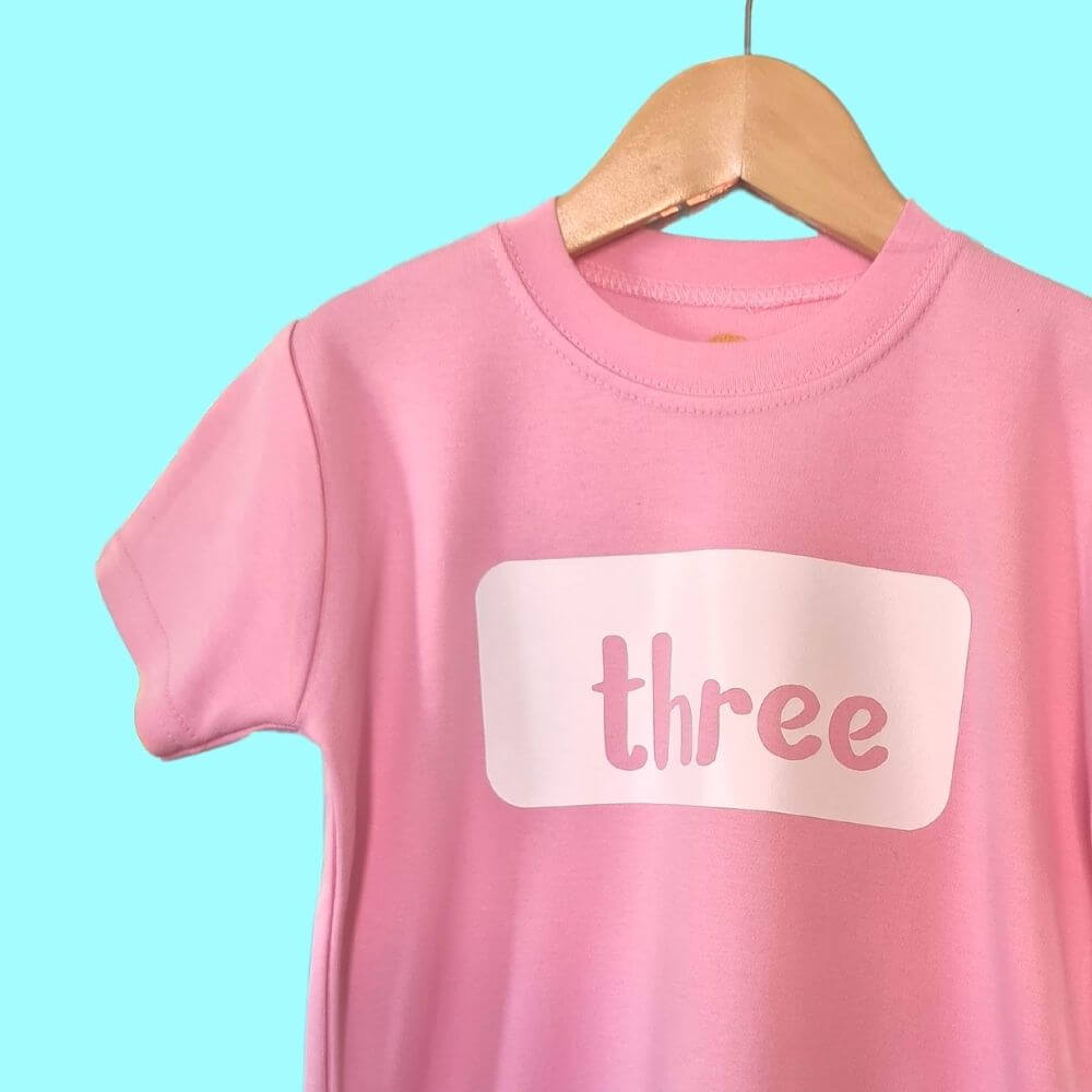 Hanging up Pale Pink t-shirt with white 'Three' logo. 3rd Birthday tshirt from The Joyful Rebel.