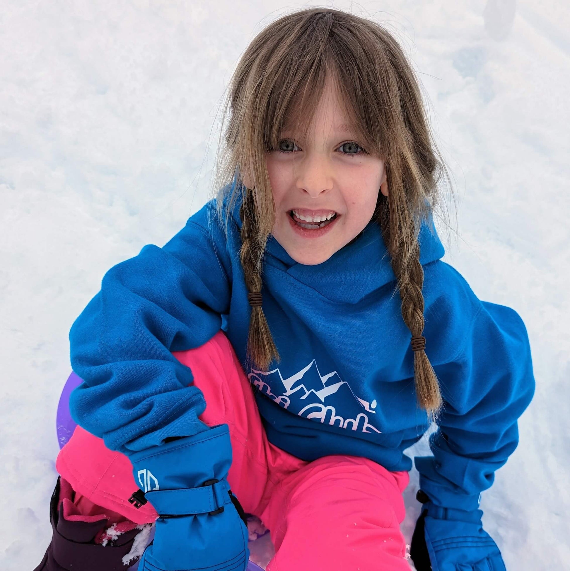 Happy little girl wearing blue ski sweatshirt sat in snow.