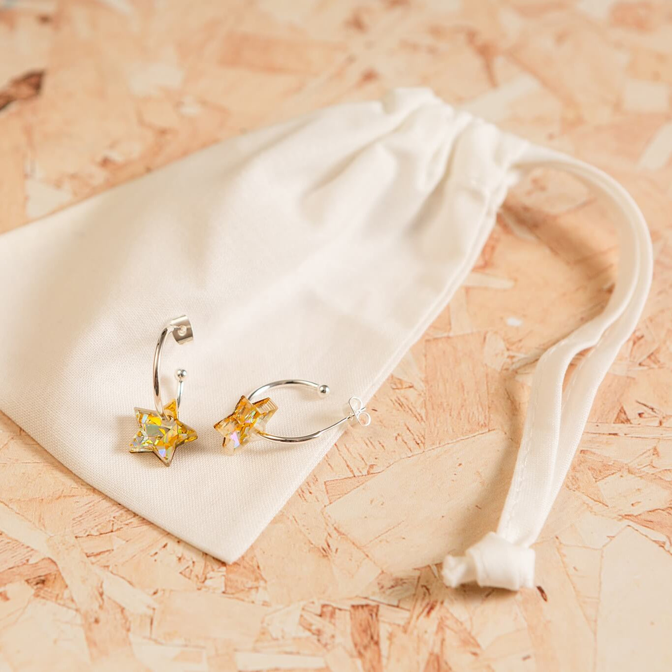 Pair of gold earrings on a white drawstring bag against a wooden background