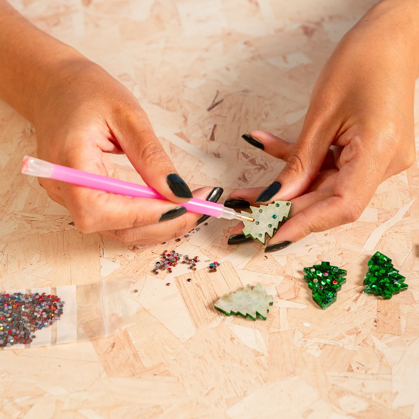 Person decorating small green tree-shaped objects with colorful embellishments on a light surface.