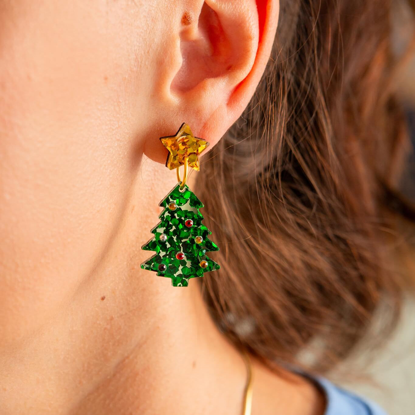 Close-up of a person wearing a gold star earring with green Christmas tree-shaped charms.
