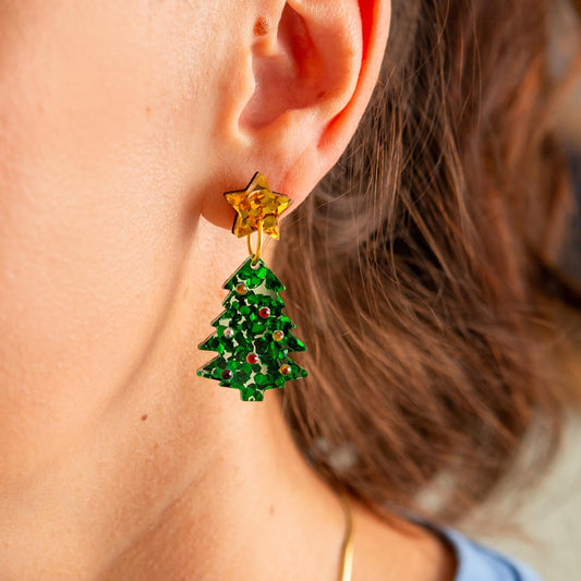 Close-up of a person wearing a gold star earring with green Christmas tree-shaped charms.