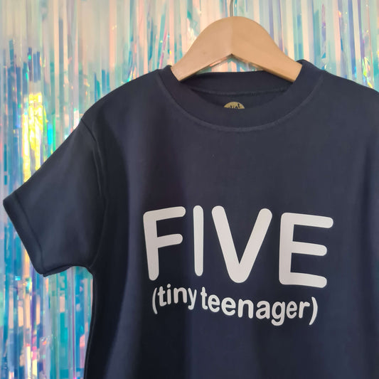 Navy Blue t-shirt hanging up on a hook. The t-shirt has a white logo 'FIVE (tiny teenager)