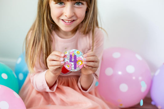 Young girl wearing a pink dress. She is holding a liberty print birthday badge with the number 4.