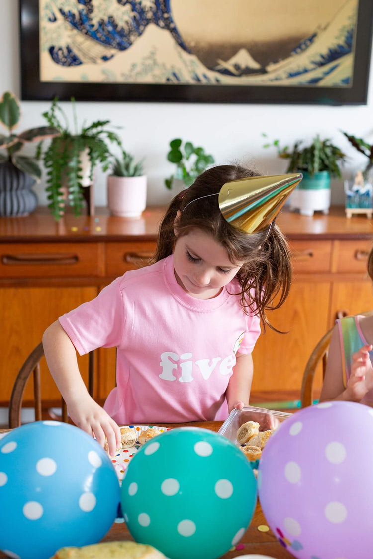 Young girl wearing a birthday tshirt with balloons and party hat