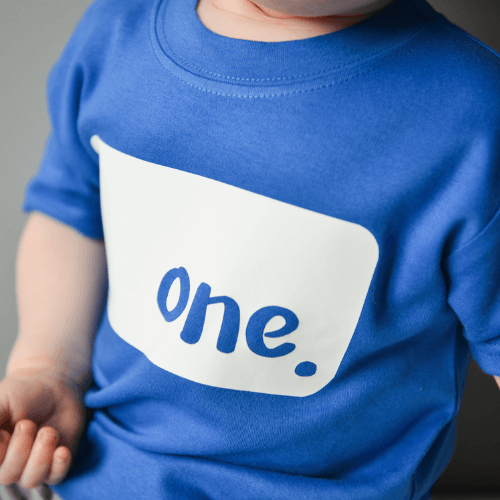 Toddler wearing The Joyful Rebel birthday royal blue tshirt with white 'ONE' logo