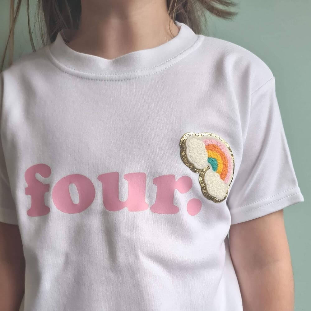 child wearing a white t-shirt with pink 'FOUR' text and embroidered rainbow by The Joyful Rebel