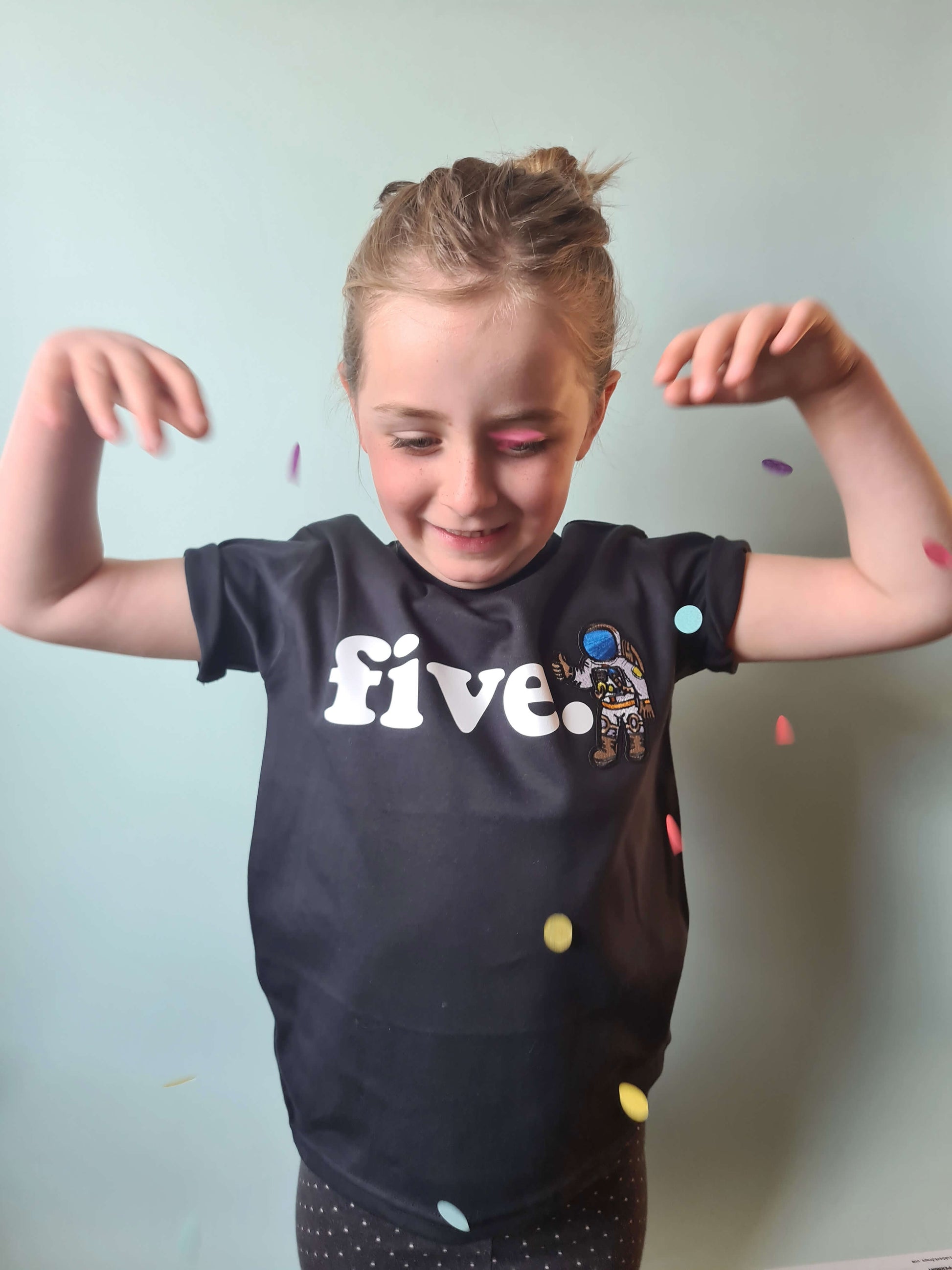 child throwing confetti in the air wearing black space birthday tshirt