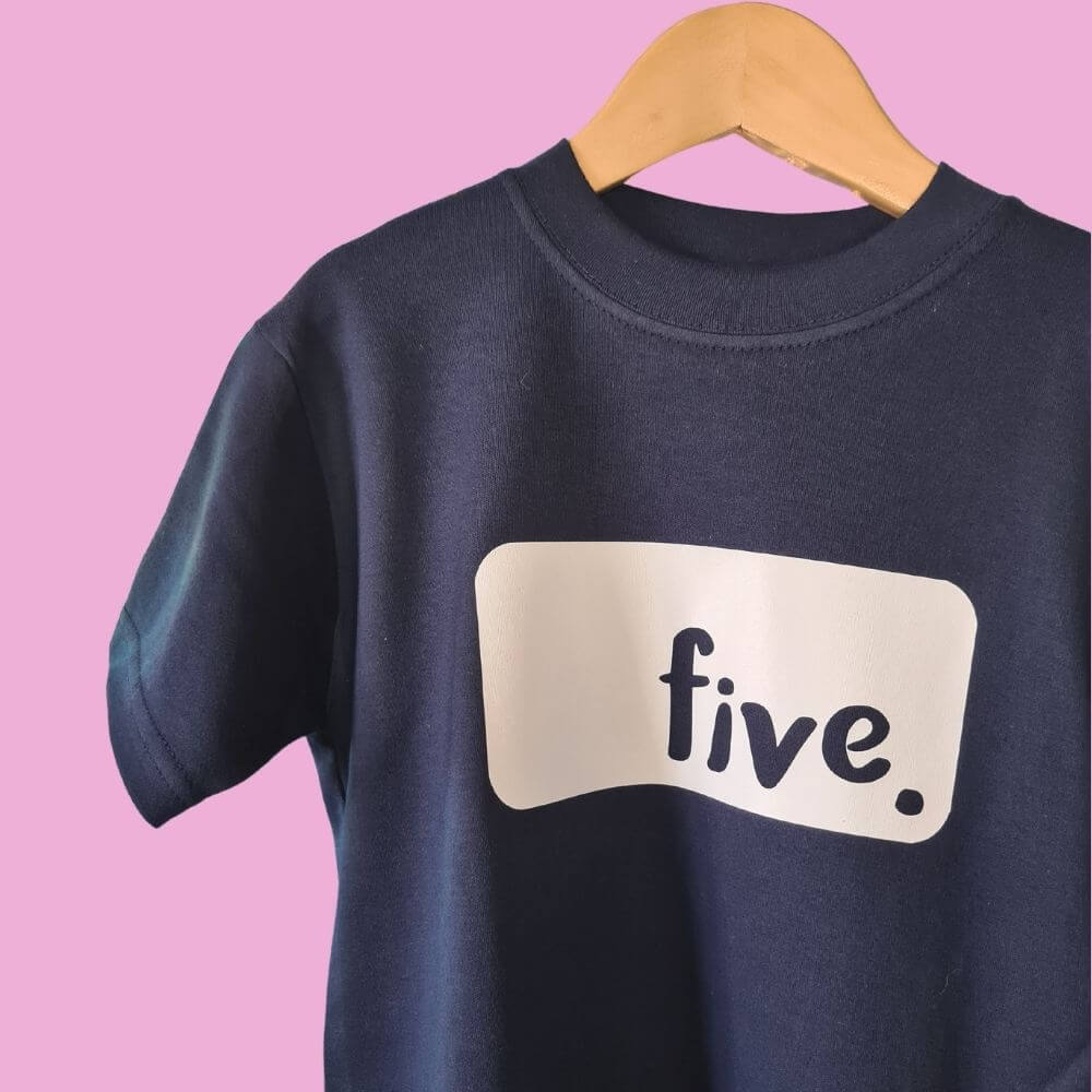Hanging navy blue birthday t-shirt with white logo text 'FIVE'. Designed by The Joyful Rebel