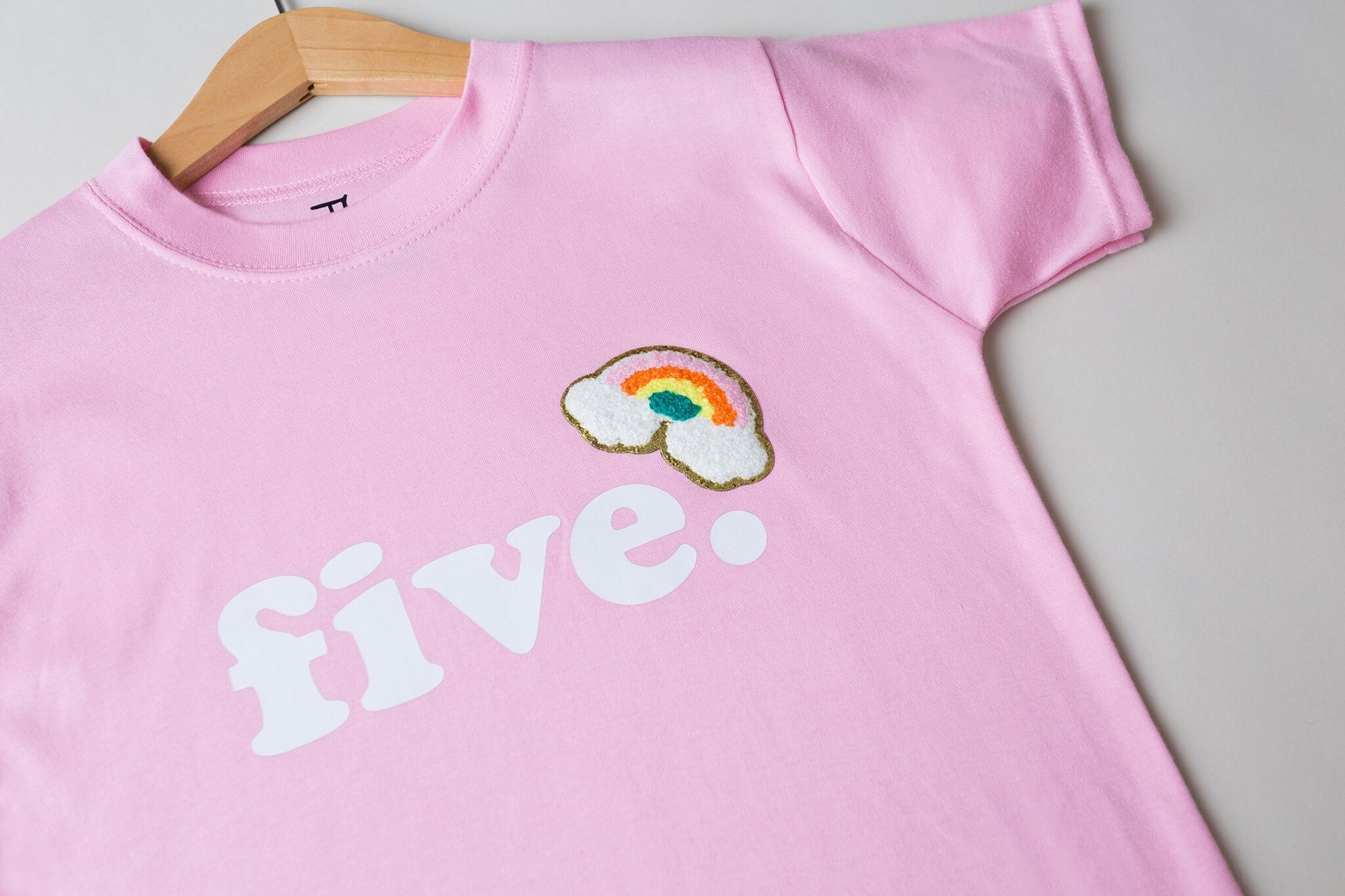 hanging pastel pink tshirt with white text 'FIVE' and embroidered rainbow