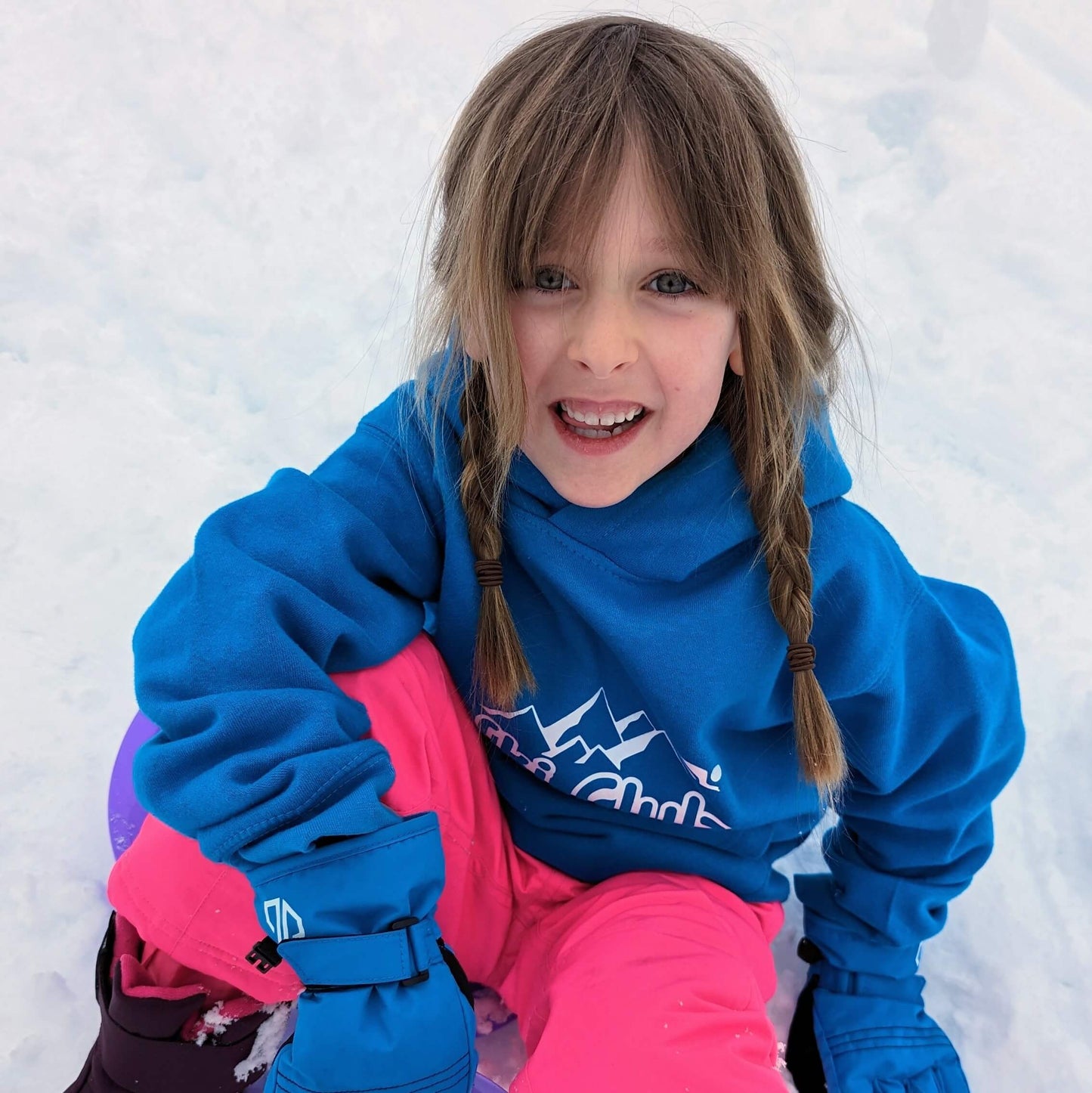 Happy little girl wearing blue ski sweatshirt sat in snow. 