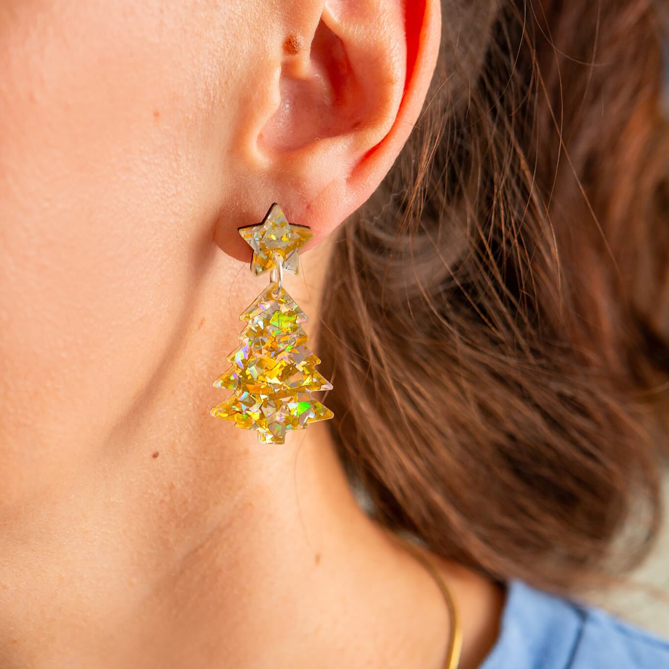 Close-up of a person wearing a colorful Christmas Tres with star-shaped earring with a blurred background.