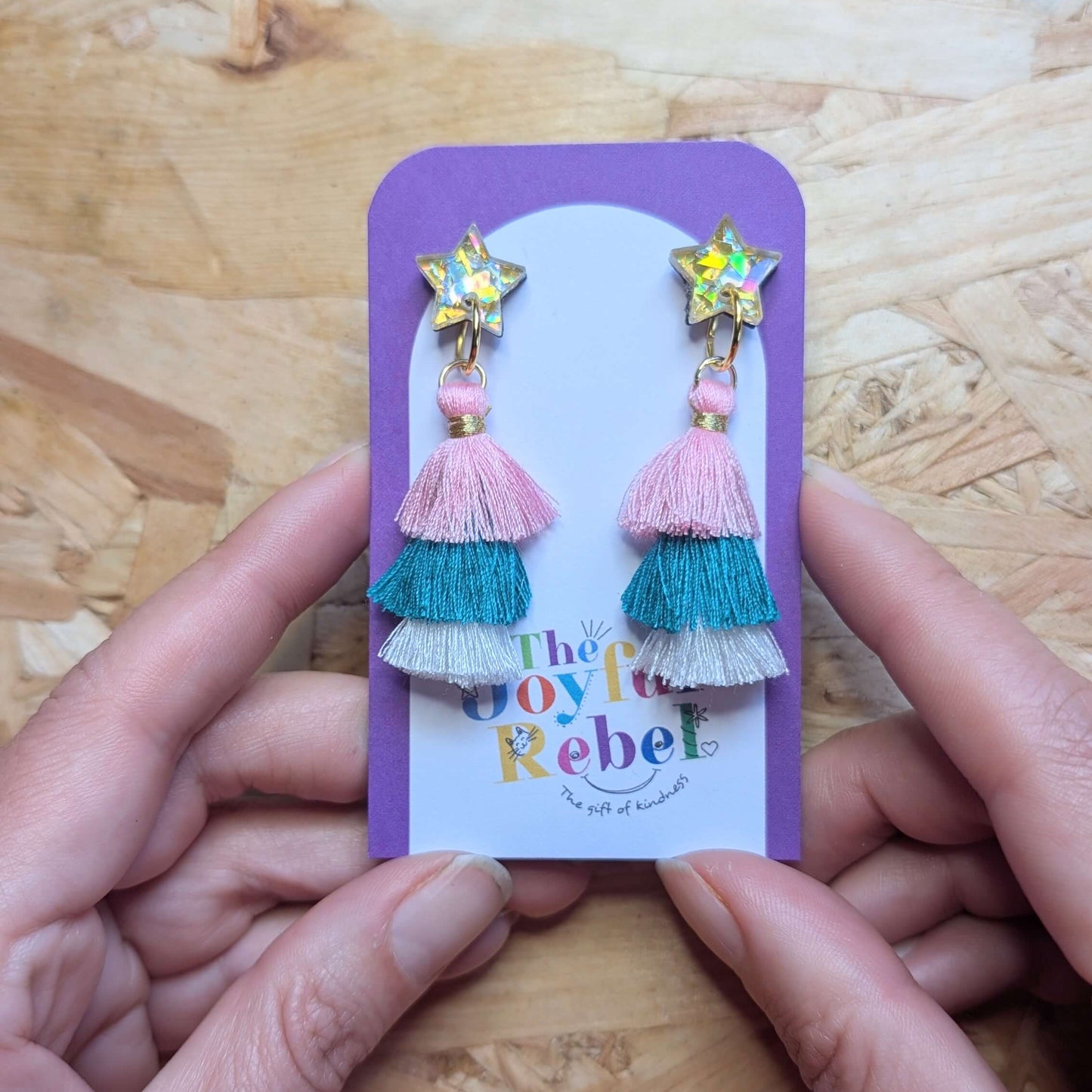 Tassel earrings on a card held by hands against a wooden background