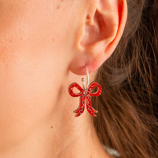 Close-up of a person wearing red bow-shaped earrings.