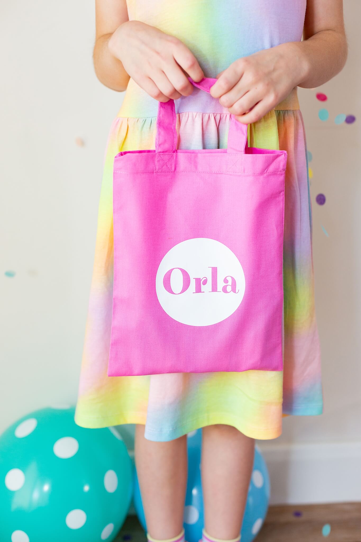 Bright pink party bag with name printed on the front in white. The party bag is being held up. 