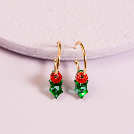 Gold earrings with red and green holly design on a light purple background