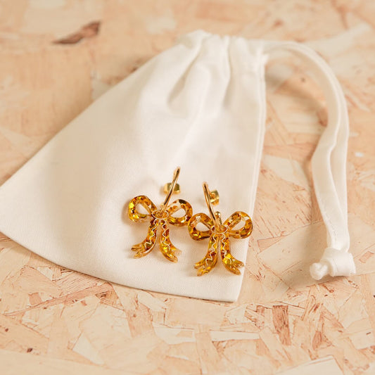 Gold bow-shaped earrings on a white drawstring bag against a wooden surface