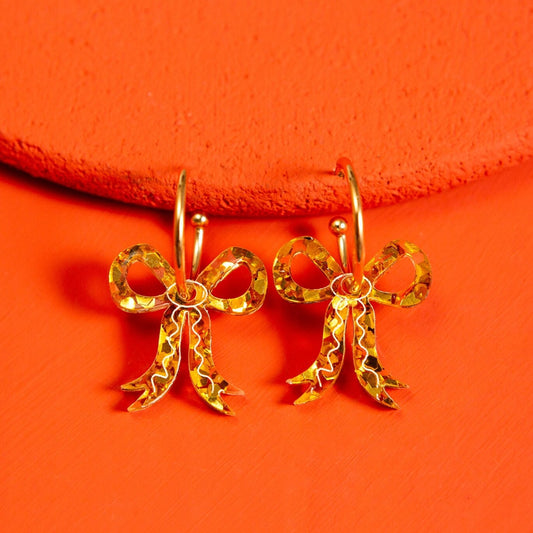 Gold bow-shaped earrings mounted on gold hoops on a red background