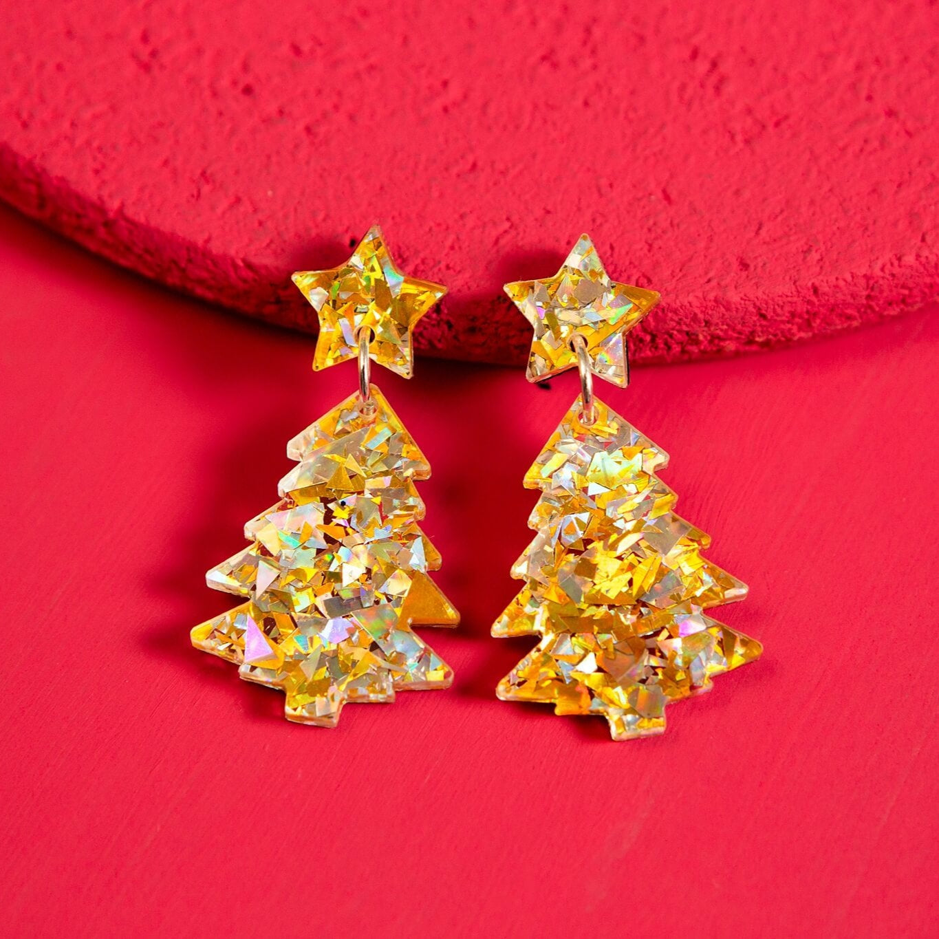 Gold and Silver Christmas tree-shaped earrings on a red background