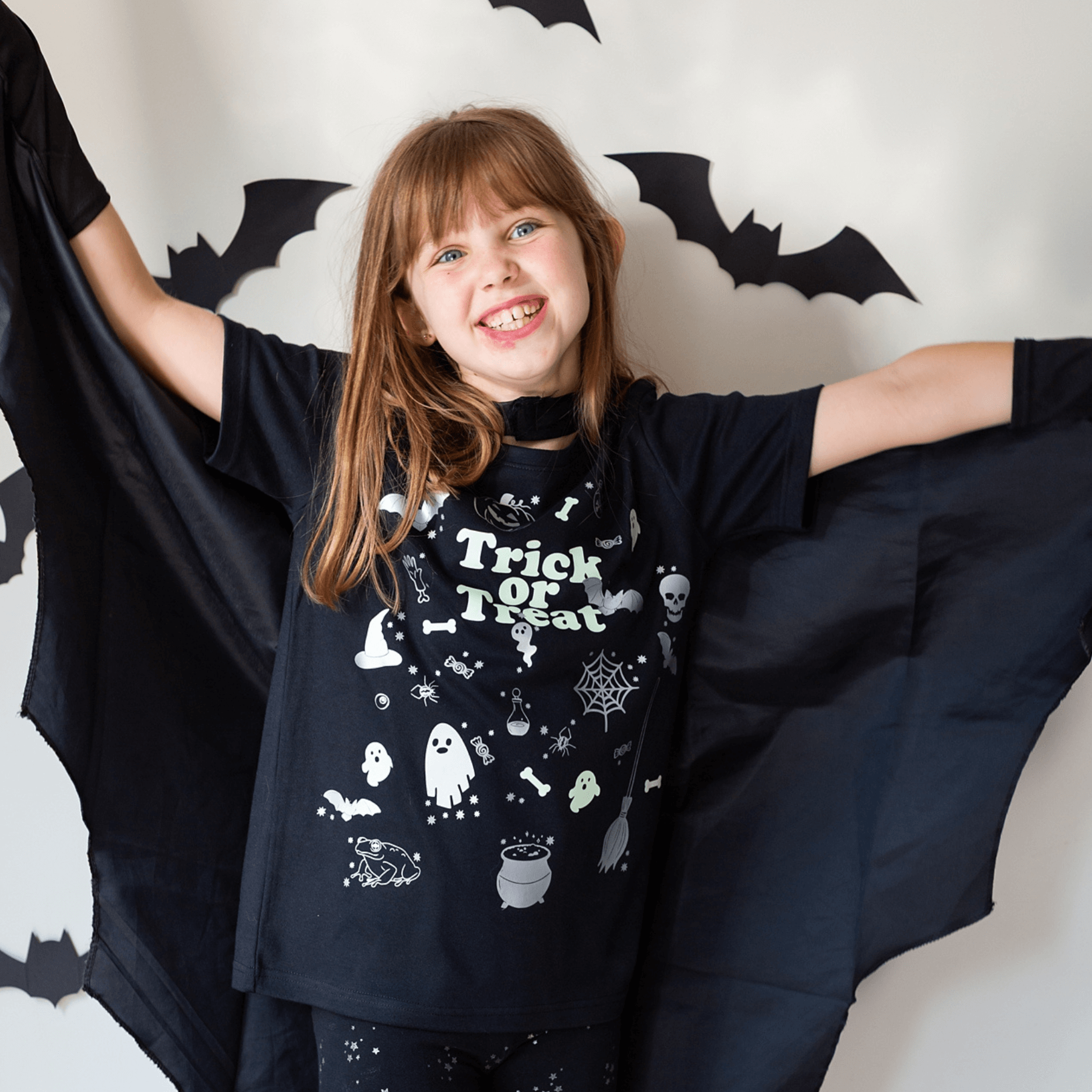 Child wearing a Halloween-themed shirt with bat wings against a decorative background