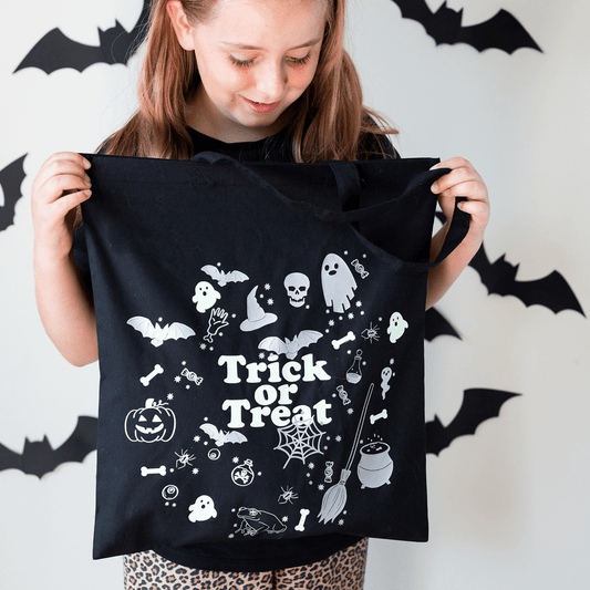 Girl holding a black tote bag with Halloween designs and 'Trick or Treat' text against a white background with black bats.