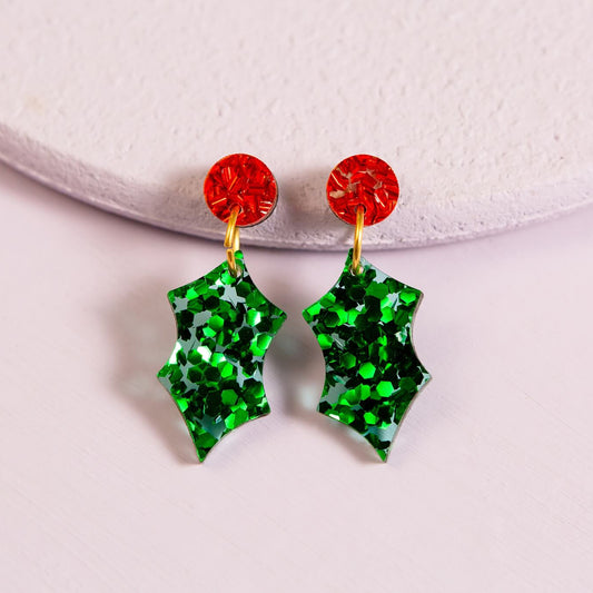 Green holly leaf earrings with red centers on a white background