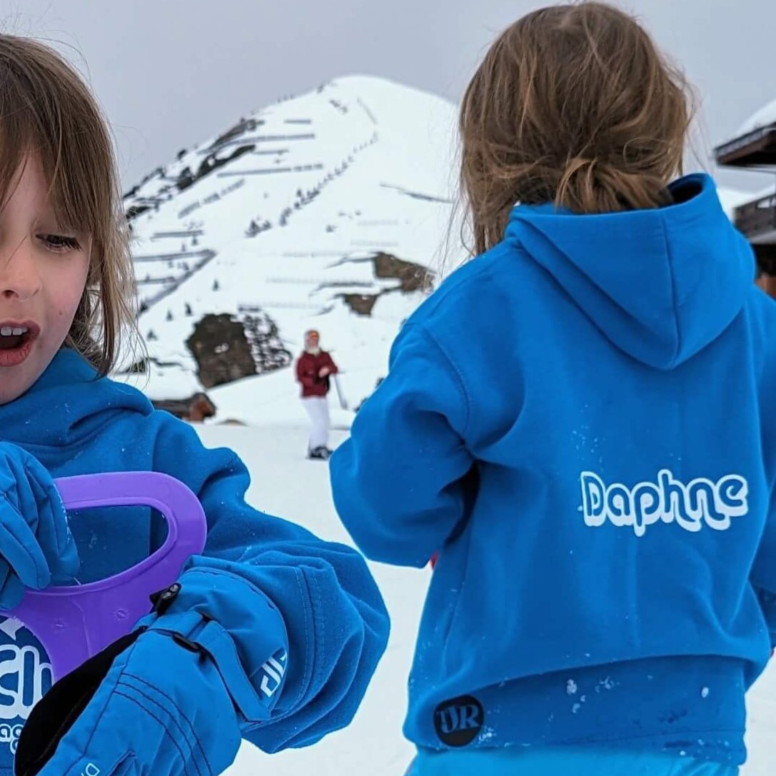 two children in the snowy mountains wearing The Joyful Rebel hoodies. Shows the options to put the name on the back of the sweatshirts