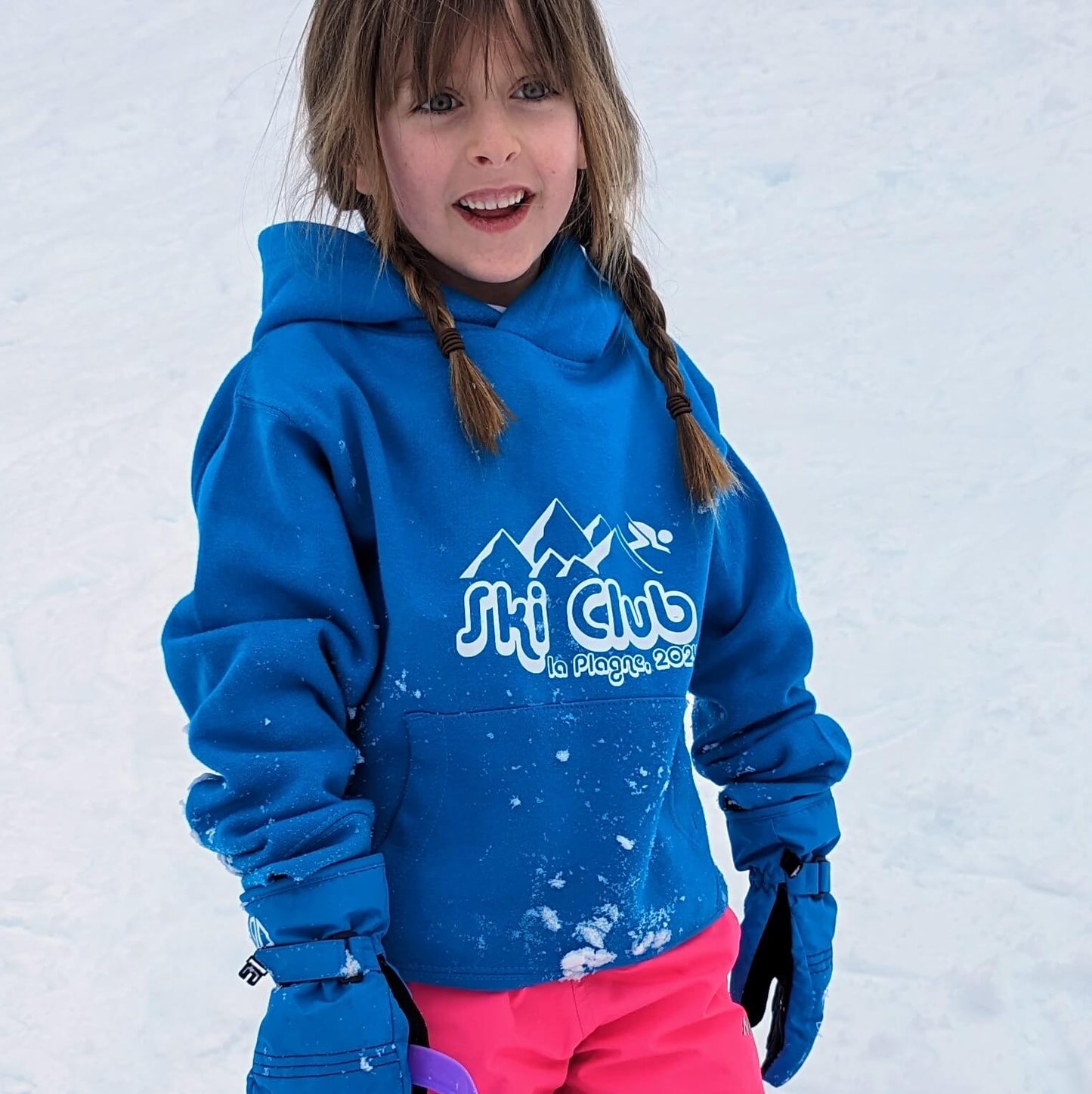 Young girl wearing a bright blue Ski hoodie. The front of the hoodie it shows 'Ski Club' text with mountain image