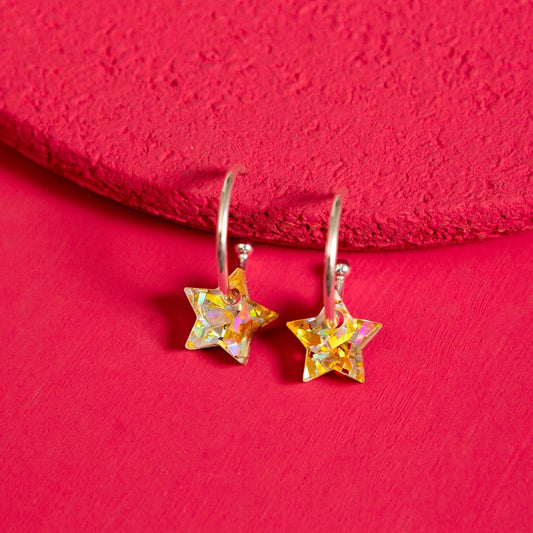 Gold and Silver star-shaped earrings on a red textured surface by The Joyful Rebel