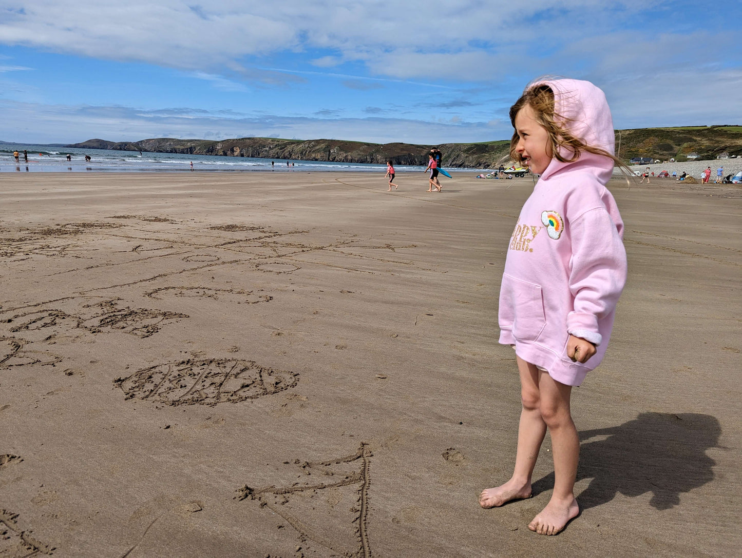 view of a sandy beach with a windy. Girls is wearing a pale pink hoodie