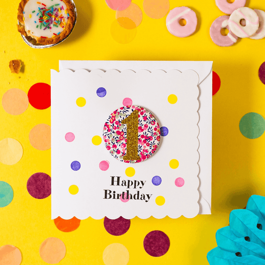 Birthday card with colourful polka dots and a floral number '1' on a yellow background with confetti.