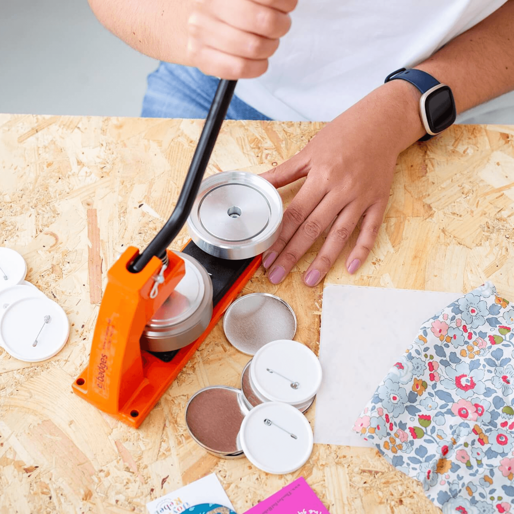 Person using a stamping tool on a wooden surface with floral paper and stamping ink pads.