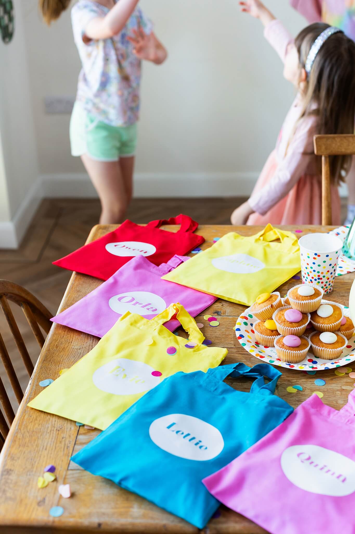 colourful personalised party bags laying on a table with cupcakes.  