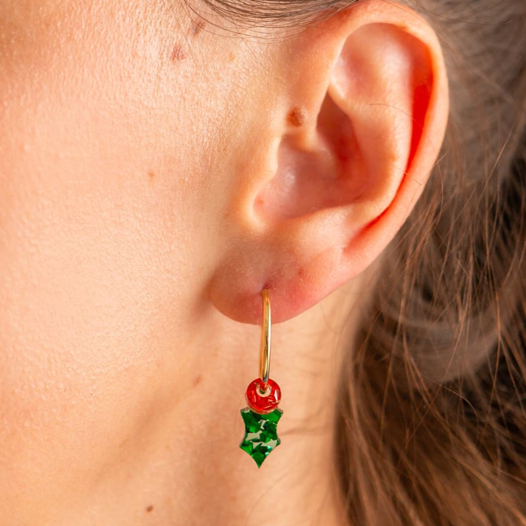 Close-up of an ear wearing a green and red holly earring with a gold hook.