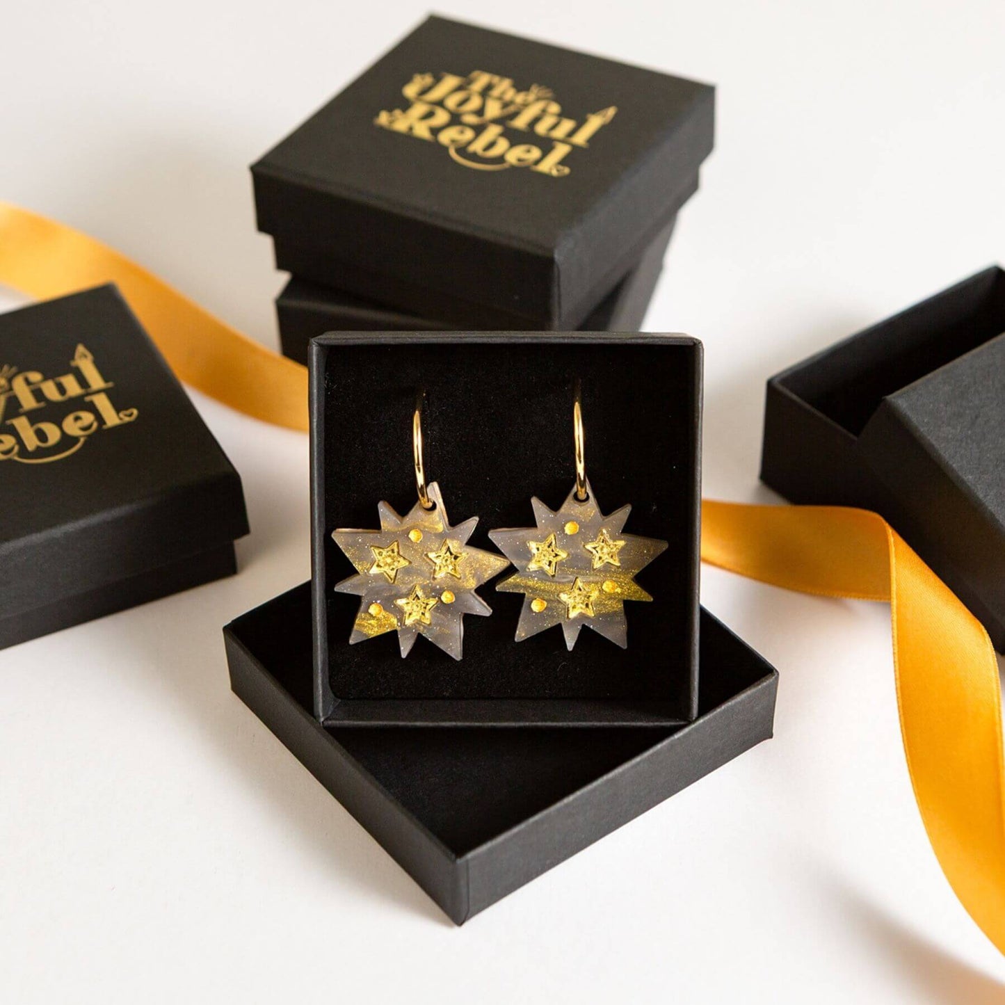 Celestial star hoop earrings presented in a black gift box with gold  branding "The Joyful Rebel"