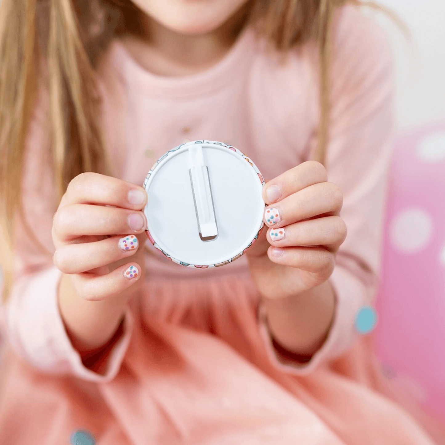 Child holding a round white object with a number one on it against a pink background