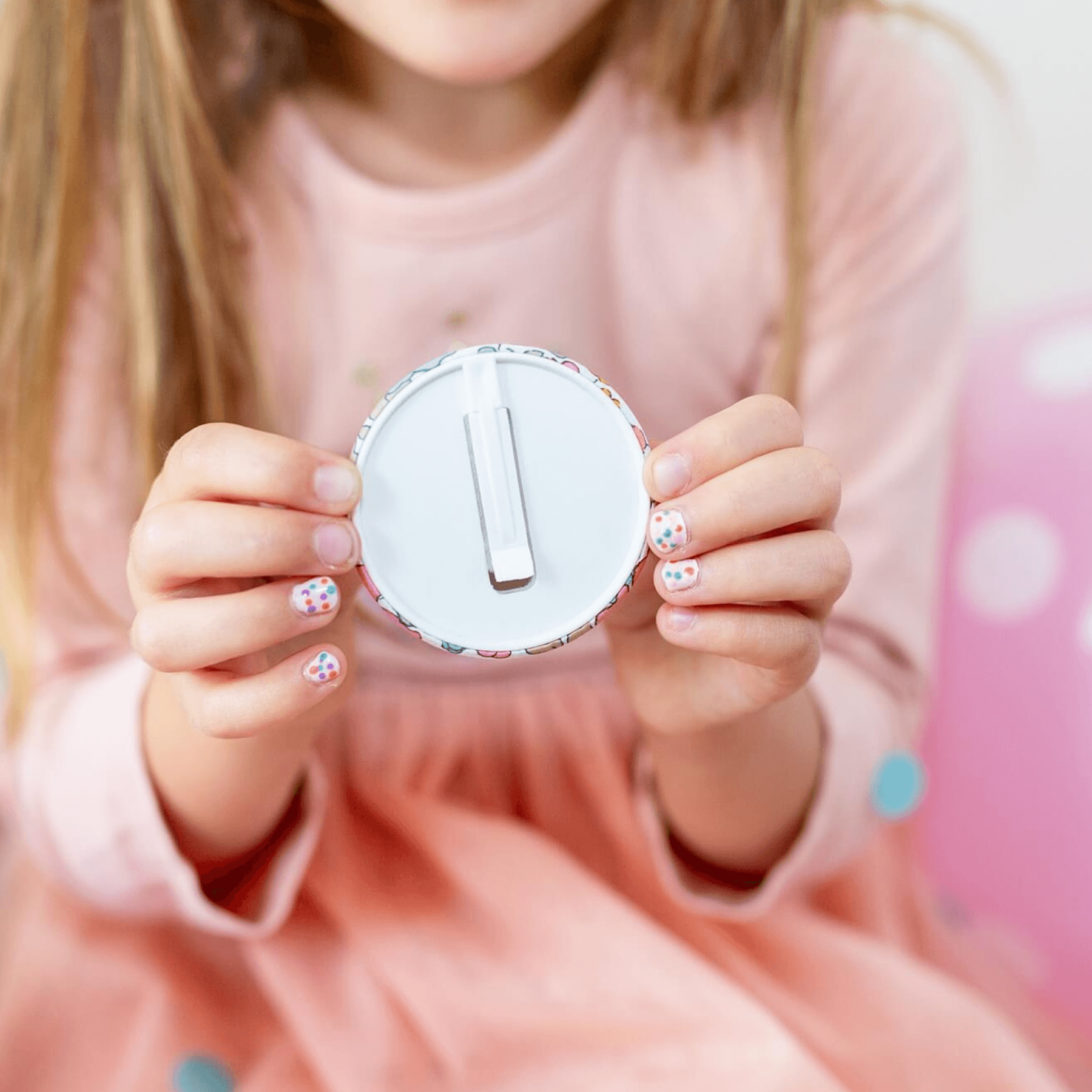 Child holding a round white object with a number one on it against a pink background