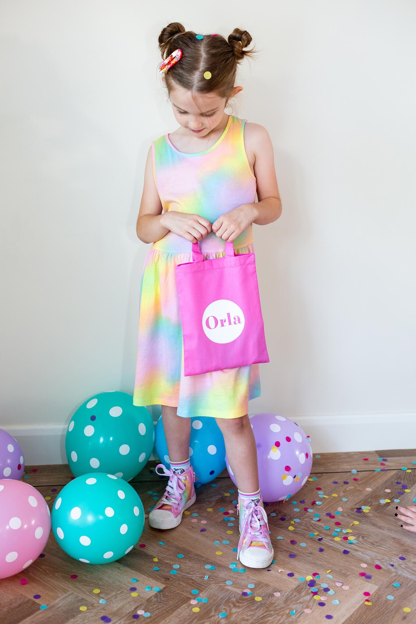 Young girl wearing rainbow dress holding a pink custom party bag