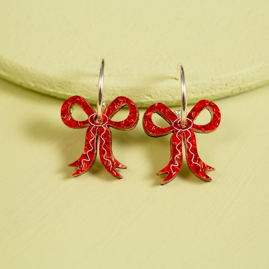 Glitter Red bow-shaped earrings on a light green background
